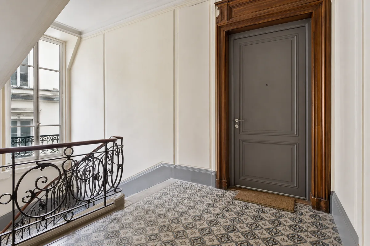 Palier d’immeuble ancien avec une porte d’entrée blindée fermée, lumière nette et sobre